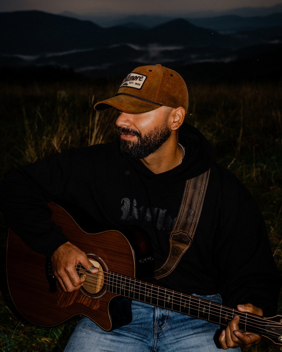 Portrait of Josh Q playing guitar at dusk with mountains behind him