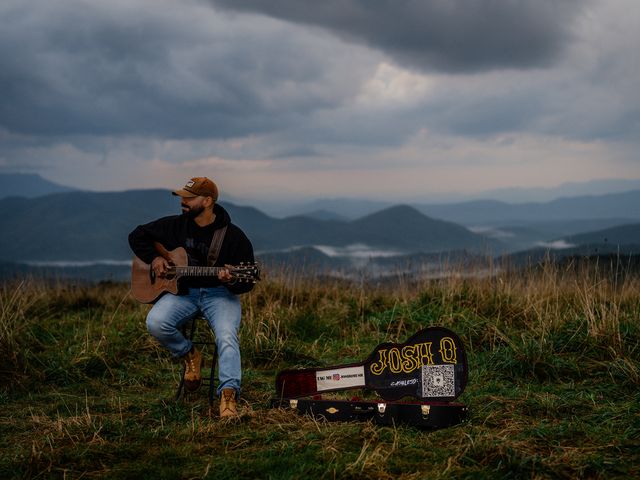 Josh Q playing at dusk beside his JOSH Q guitar case, Blue Ridge Mountains behind
