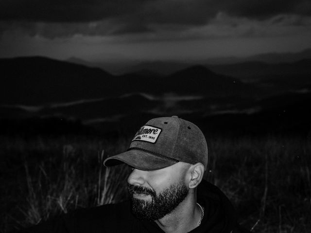Moody black and white portrait of Josh Q with his guitar at dusk