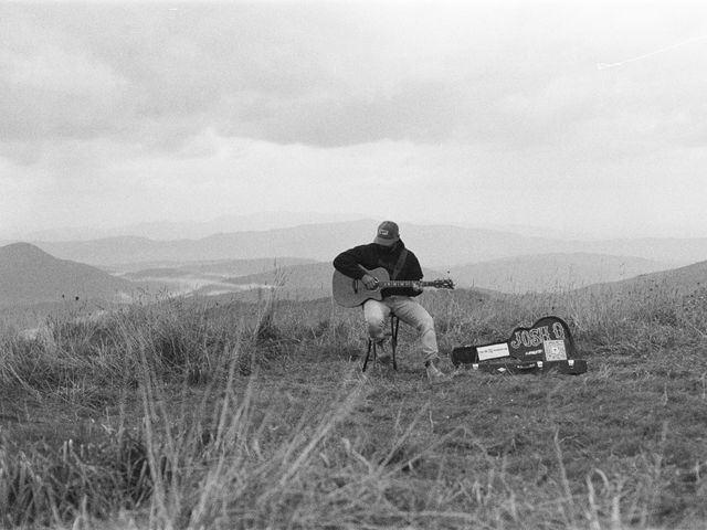 Black and white film photo of Josh Q playing beside his open JOSH Q guitar case