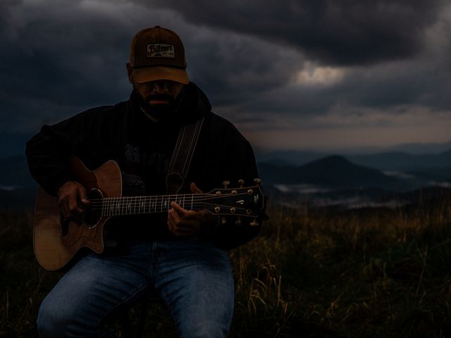 Josh Q playing guitar at dusk in a mountain meadow